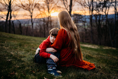 Mother and son embrace sitting on the grass outside