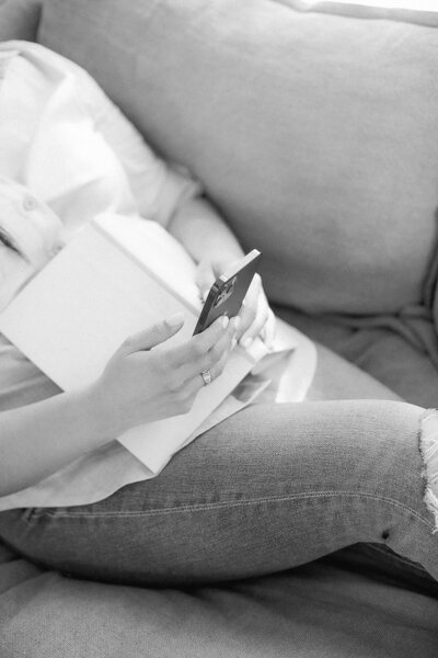Sentada con libro sobre vientre y mirando el teléfono.