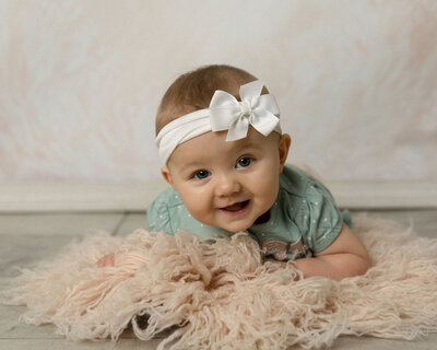 Little baby girl laying on her stomach on a pink rug smiling.