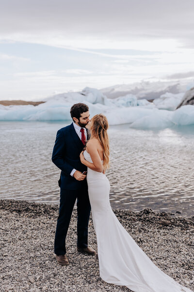 Iceland Wedding Photographer captures bride kissing groom on beach with ice