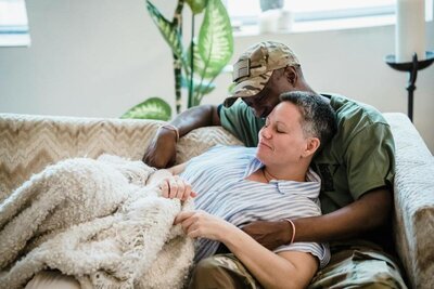 man and woman laying on the couch under a wool blanket hugging