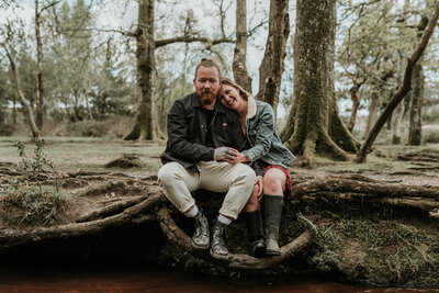 Couple cuddle next to each other on tree stump in Brockenhurst, New Forest