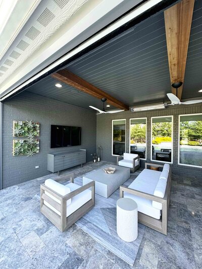 An outdoor living room designed by a professional interior designer in Frisco, featuring grey and white furniture, four large mirrors, and a TV for a comfortable and elegant space.