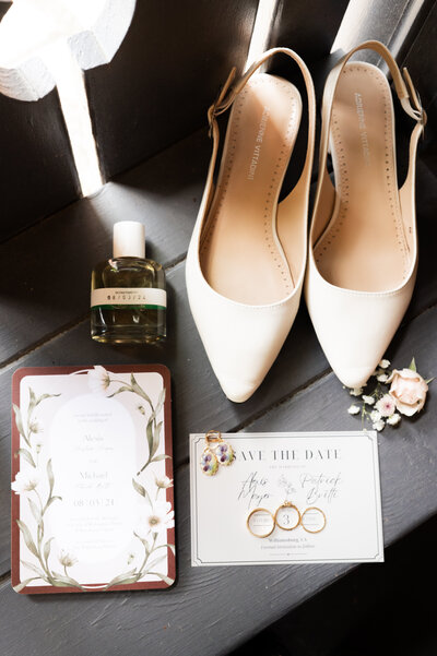 Wedding invites, jewelry, perfume, and heels laid out together