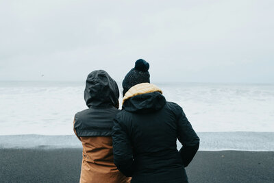 Two people wearing jackets and hats are looking at the ocean