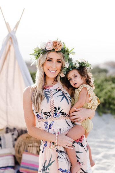 woman holding a small girl while smiling with flower crowns on their heads