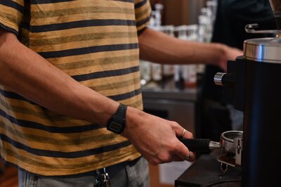 Man in a striped shirt with a black watch pulls an espresso shot