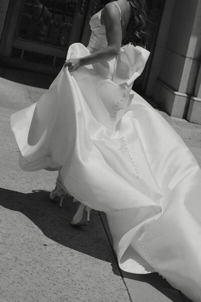 a bride's dress fluffing in the wind as she runs in black and white