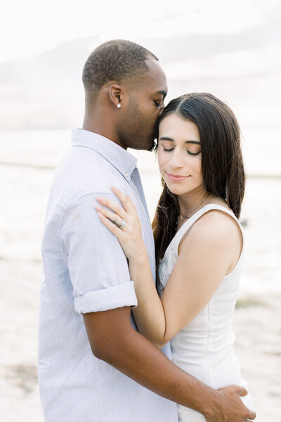 Man kissing woman's temple on the beach during an engagement portrait session in Tampa, Florida