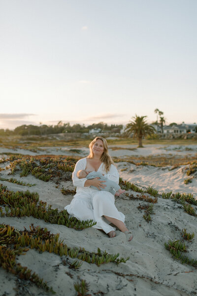Molly, a San Diego photographer, standing on the beach with her partner and their baby, smiling at the camera during a family portrait session