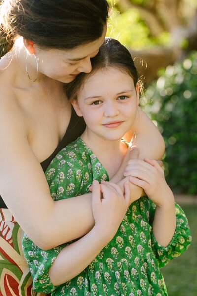 A mother holds her young daughter, wearing a green dress.