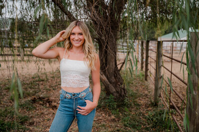 Teenage girl poses under a willow tree smiling.