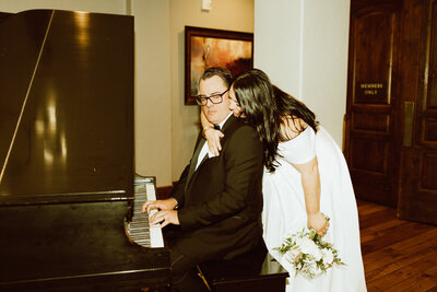 bride kissing groom's cheek while he plays piano