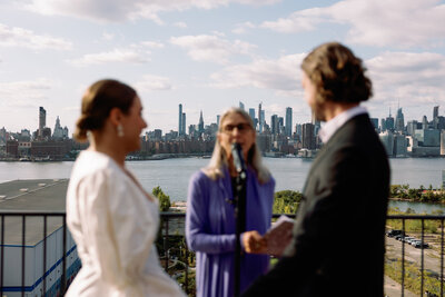 wedding photography of blurry bride groom and officiant on NYC rooftop with the city behind them in focus