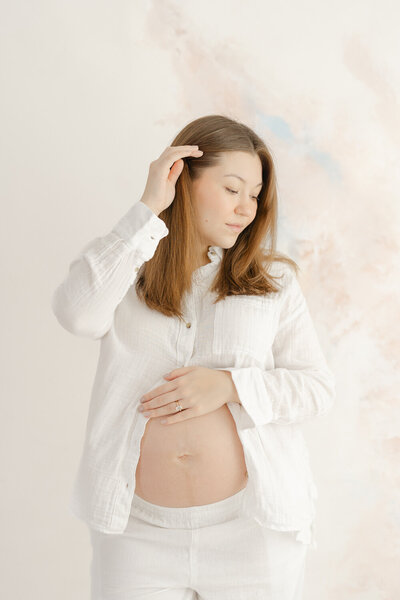 expecting mom fixing her hair during studio maternity photo in Gainesville, Virginia