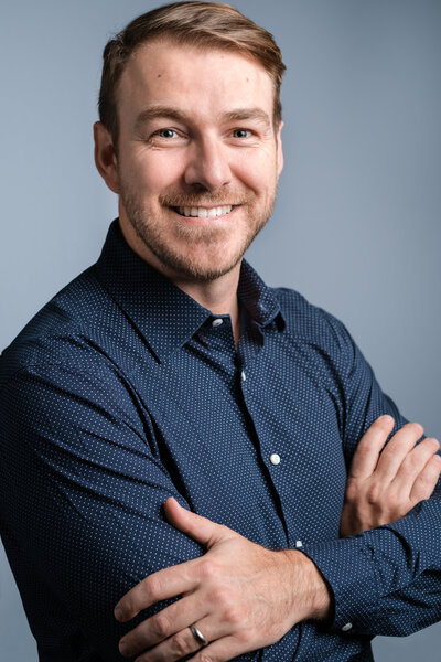 Corporate event photographer wears a blue shirt and smiles at the camera