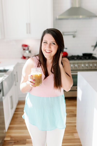 Woman smiling in kitchen with coffee in mason jar