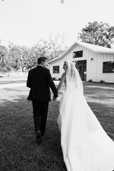 Black and white documentary wedding photography of couple holding hands and running away.
