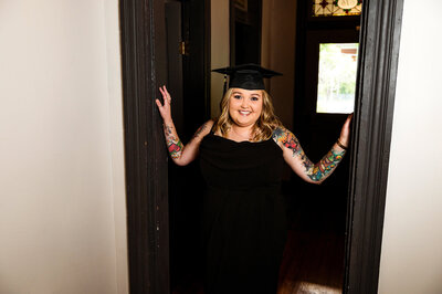 Online degree graduate wearing her cap and smiling in the doorframe of a private residence