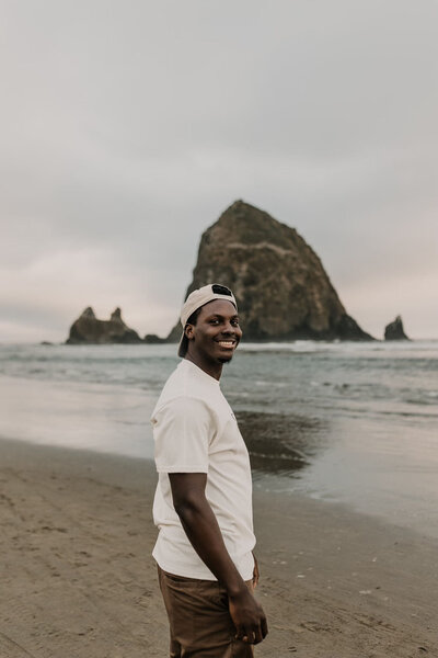 David Pitchford wearing a white tshirt and backwards hat smiling at camera in front of haystack rock