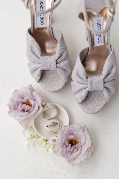 Black and white photo of wedding shoes with rings on a tray in between the shoes