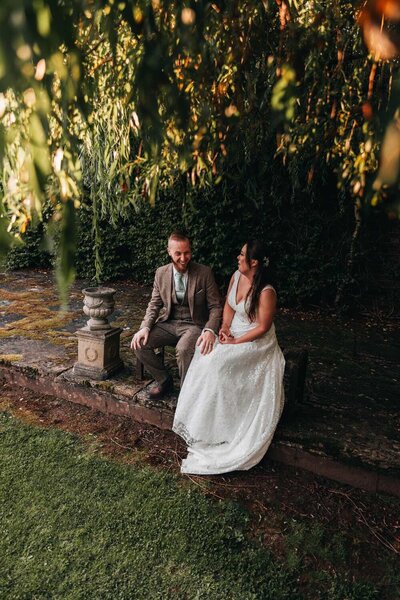 Bride & Groom sit together smiling under tree