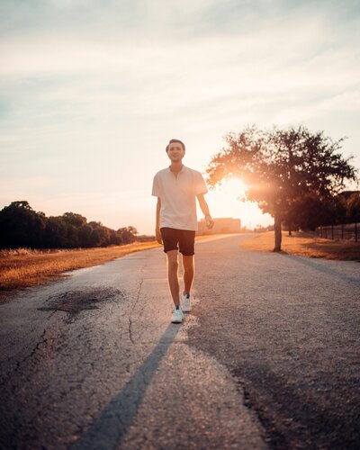 Man walking along road with sunset behind him