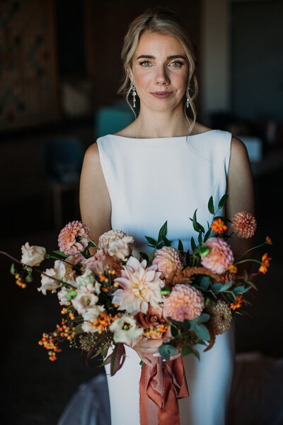 Blonde bride in elegant gown softly smiles at the camera with a large spring bouquet in hand