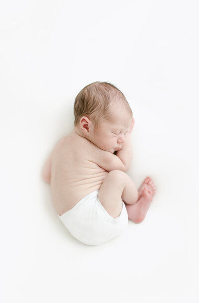 newborn curled up on white background