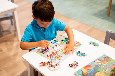 A young toddler boy playing with a vehicle puzzle during half-day care at The Nest, a natural learning center in Surf City, NC