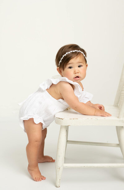 One year old baby girl standing with a chair in white background