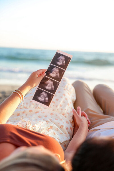 Maternity photo of pregnant woman by the ocean in San Diego holding her ultrasound.
