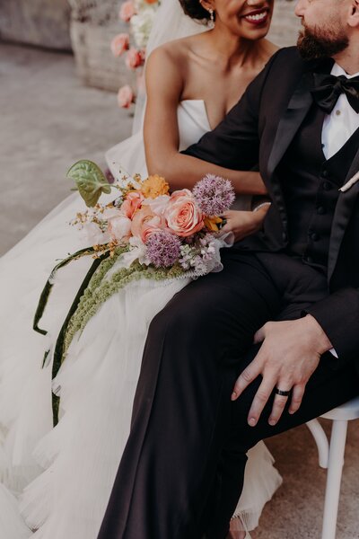 Bride snuggles into groom while holding her colorful bouquet