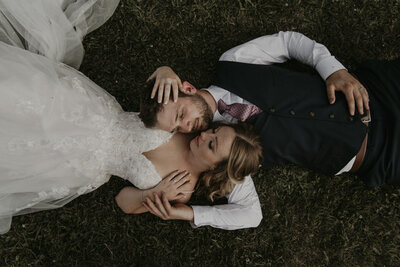 wedding couple standing outside in front of a glass wall of square window panes. They are holding hands side by side and looking off in opposite directions.