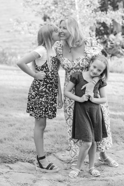 Daughter kissing Mom on the cheek while Mom holds hands with other daughter | Family Photography Session taken by Maine Photographer