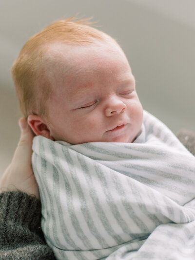 Newborn baby boy with red hair being held in his Southern Maryland nursery.