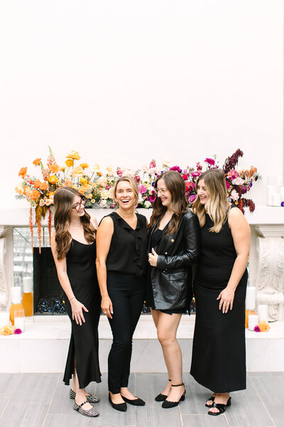 A group walks confidently out of the front entrance of SoHo63, a Chandler wedding and event venue, under its signature white stucco arch and bold signage. The sunny exterior and wrought iron doors highlight the venue’s stylish presence in Downtown Chandler.