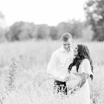 A pregnant woman and her husband smile at each other in a flower field