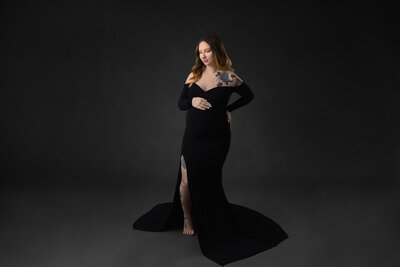 prenant woman in long black off the shoulder dress with her hand resting on her belly