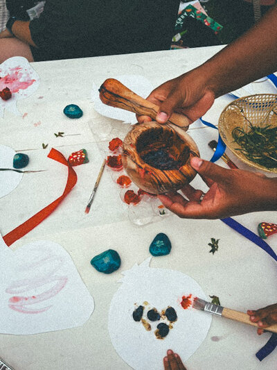 Close-up of hands crafting with natural materials like leaves, stones, and wooden bowls, part of the Gardens program for ages 2.5-6.