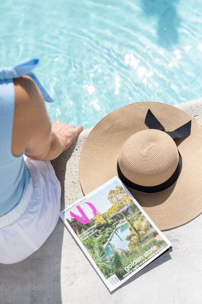 Tara enjoying a peaceful moment by the pool, reading Architectural Digest, embodying her passion for design and relaxation while connecting with the community in Queen Creek.