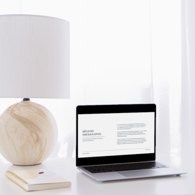 Laptop on desk displaying a brand messaging document, styled with soft natural light and neutral workspace decor