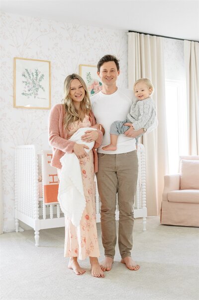 Family holding newborn in a  pastel pinkgrandmillenial nursery