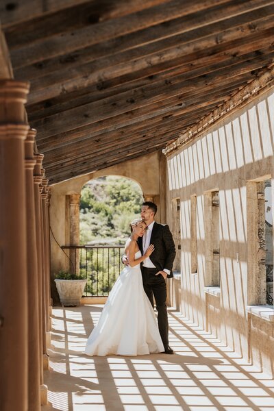 a bride and groom snuggling under a pergola