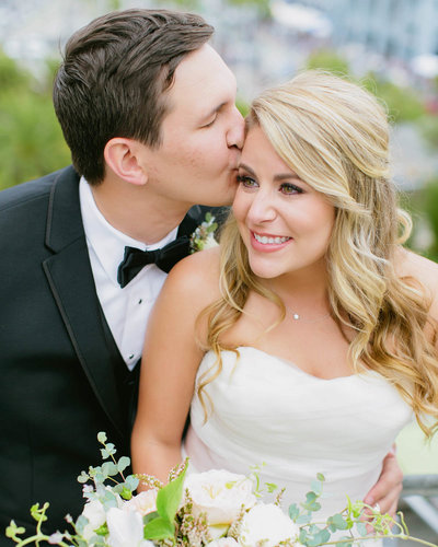 Groom kisses Bride head as Bride smiles looking to her right