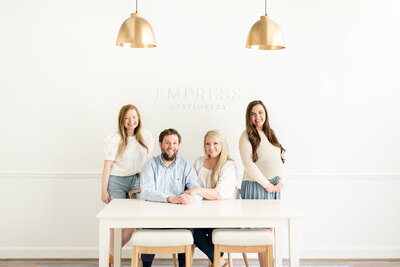 Headshot of 4 person team at a desk in front of a wall with the Empress Stationery logo