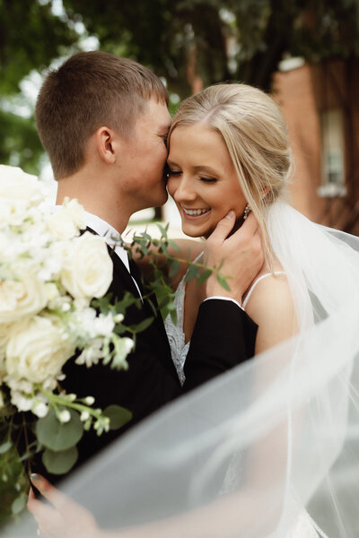 The groom whispering something sweet into his brides ear while she giggles with a beautiful shot of the brides veil and bouquet.