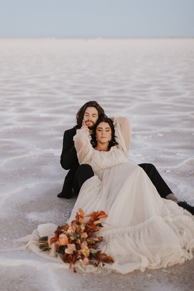 Couple cuddled up on the salt flats, the sun setting behind them, highlighting the dramatic landscape during their travel elopement