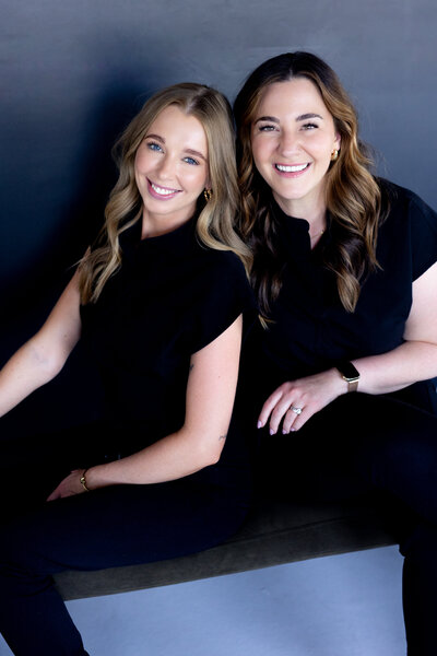 Allie and Sarah facing the camera wearing black scrubs