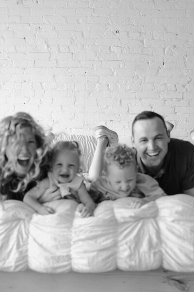 Young family snuggles on bed with white duvet cover during Kinfolk sessions by Minnesota photographer